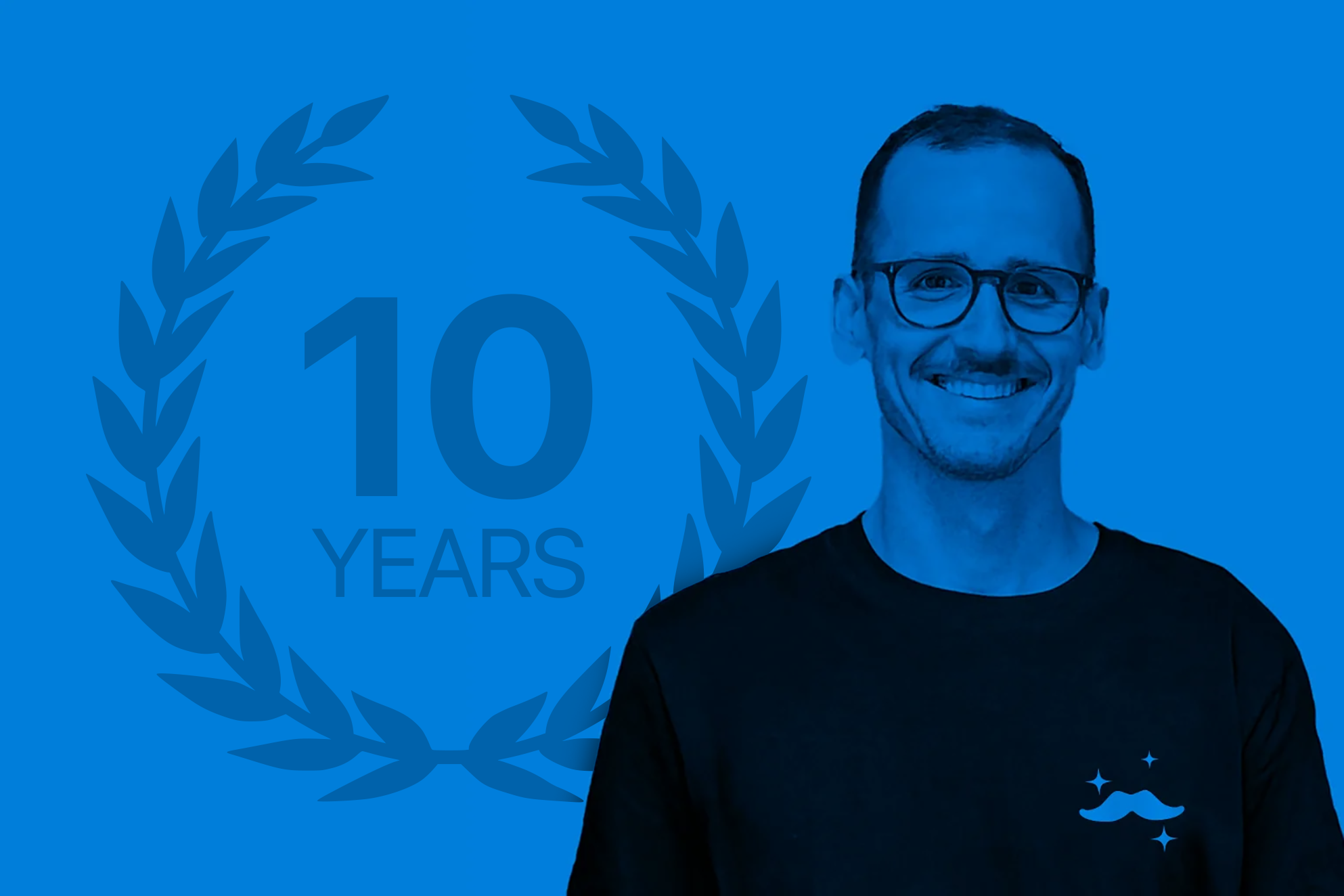 Stefan Malzner, founder of Franz, photographed in a cobalt blue duotone with the Franz mustache logo on his shirt, marking ten years of Franz
